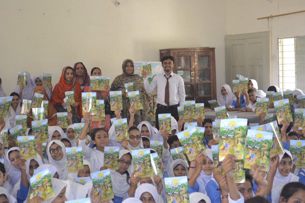 Teacher in Pakistan with classroom full of girl students, holding up Way to Happiness booklets