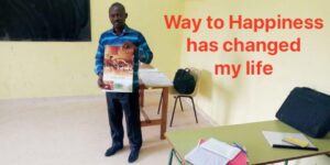 Tiade a teacher in Ivory Coast holding Way To Happiness poster, Happiness and Self Improvement